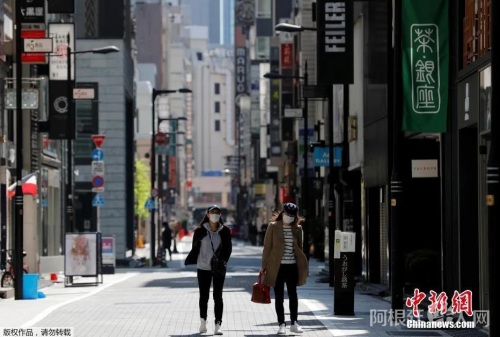 日本东京,戴口罩的女士走过空无一人的购物区。 日本东京,戴口罩的女士走过空无一人的购物区。